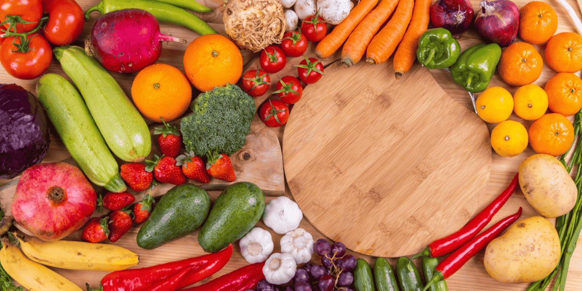 a variety of colorful fruits and vegetables displayed with a round wooden cutting board