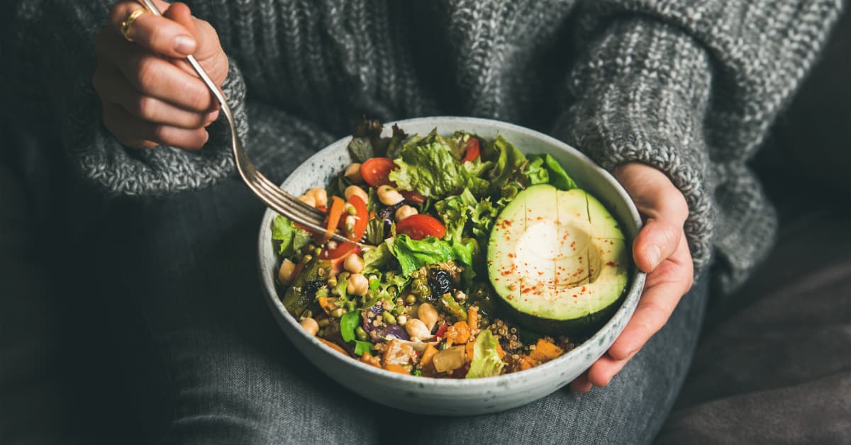 a woman in a gray knit sweater eating a high-protein bowl full of fibrous vegetables 