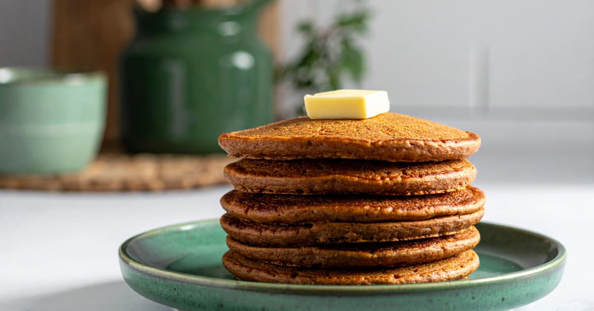 a stack of whole wheat gingerbread pancakes topped with a pad of butter on a green ceramic plate