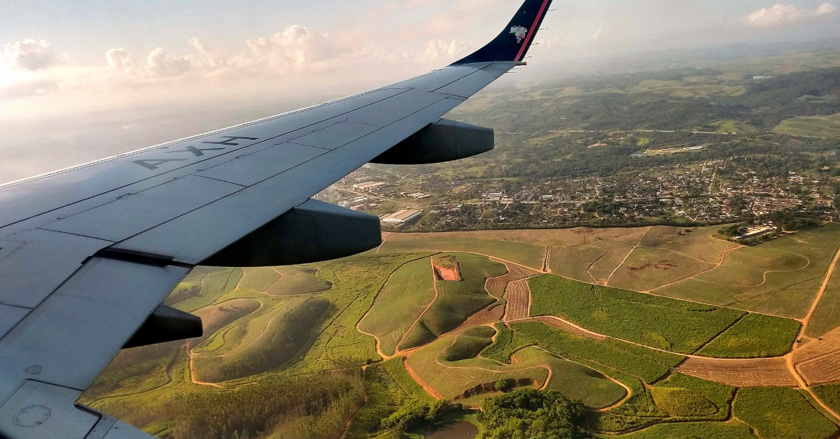 an airplane flying over grassy fields outside of a vacation city