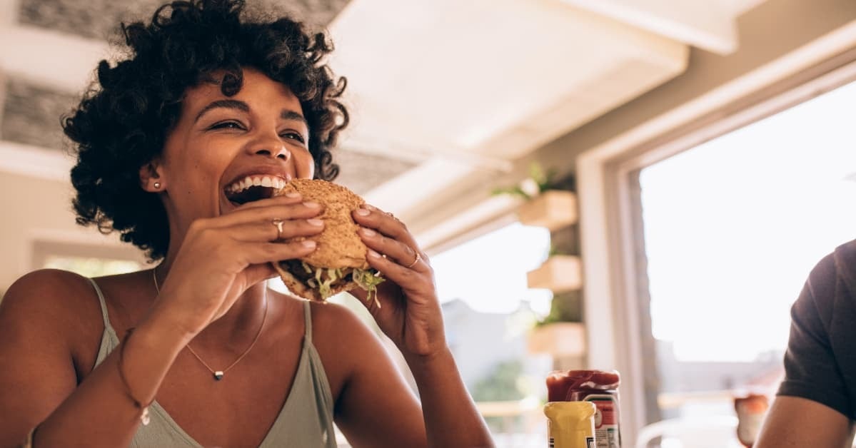Young woman confidently eating a burger at a table with friends
