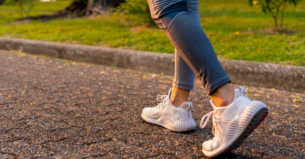 woman in white sneakers and gray leggings walking at sunset on a paved walkway