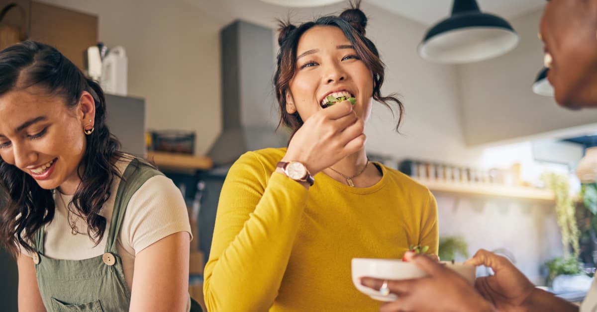 woman in a yellow shirt eating strawberries in the kitchen with her two female friends