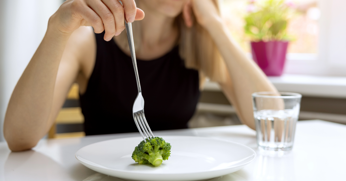 a woman with a black top eating a piece of broccoli 
