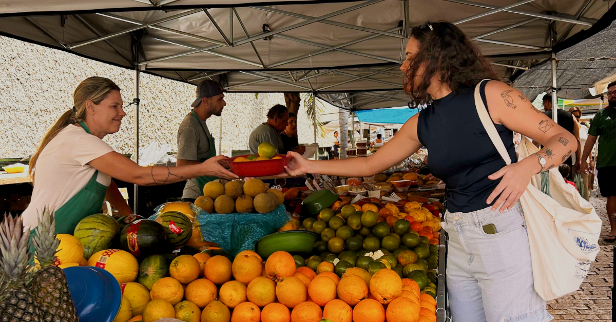 a woman purchasing fruit at a farmers market from a local vendor