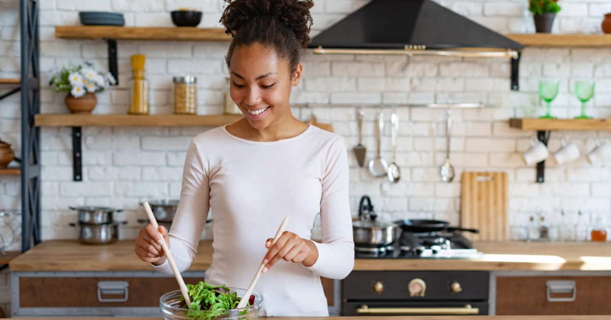 young woman in her kitchen tossing a salad in a bowl with wood tongs