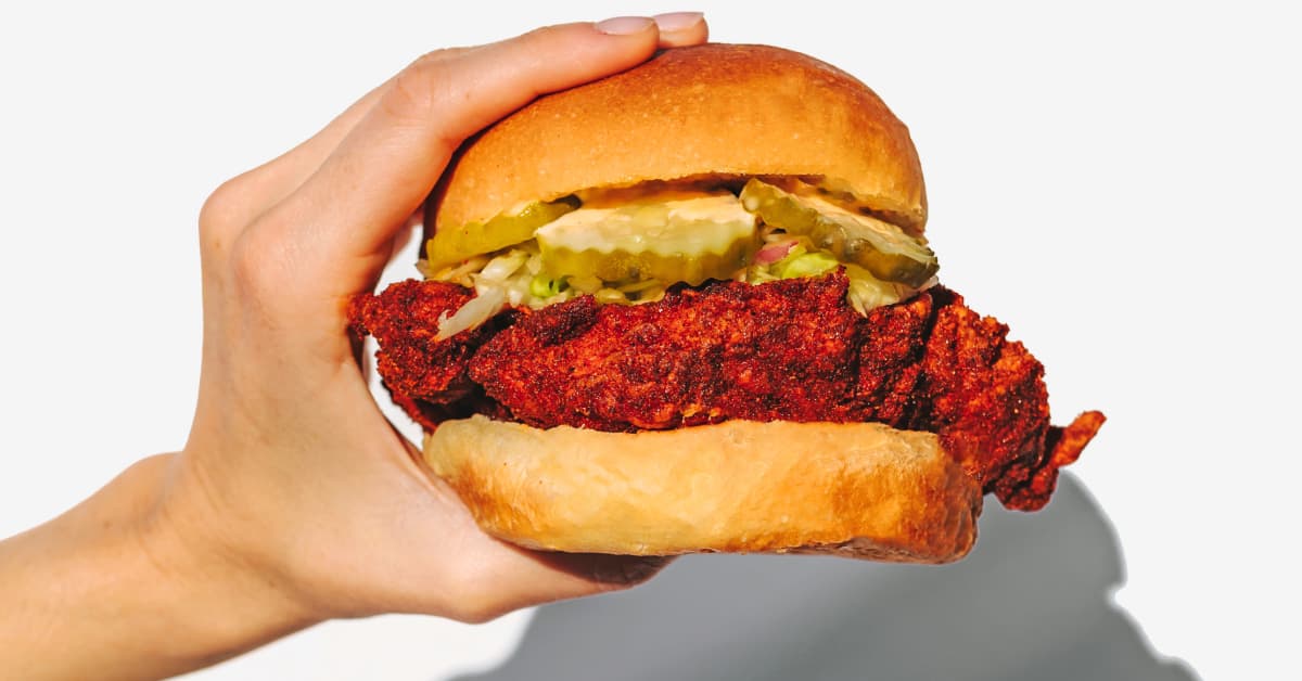 a hand holding a chicken sandwich with pickles