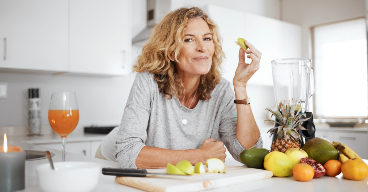 a perimenopause woman in her kitchen eating fruits and vegetables for proper nutrition