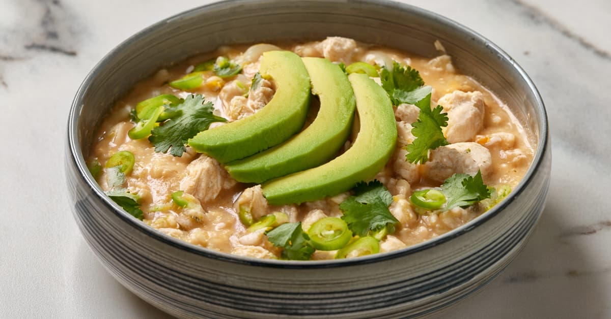 a ceramic bowl full of white chicken chili topped with avocado, jalapeno, and cilantro 